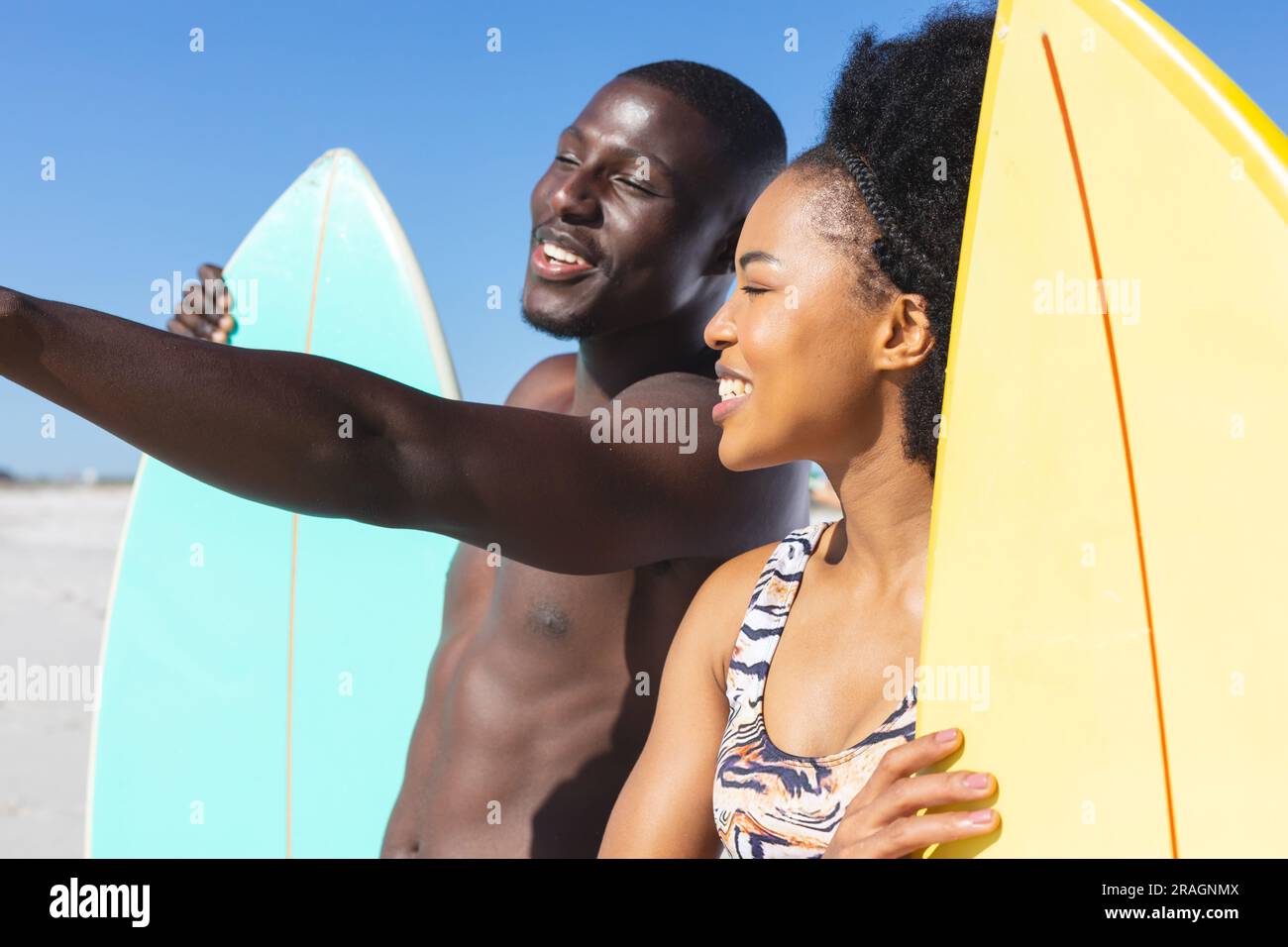 Happy african american couple holding surfboards standing on sunny beach talking Stock Photo