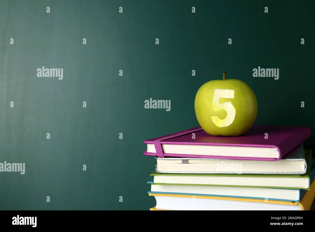 Apple with carved number five as school grade on books near green chalkboard, space for text Stock Photo