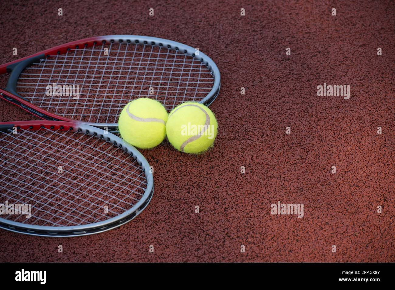 Two yellow tennis balls and two racquets on hard tennis court surface ...
