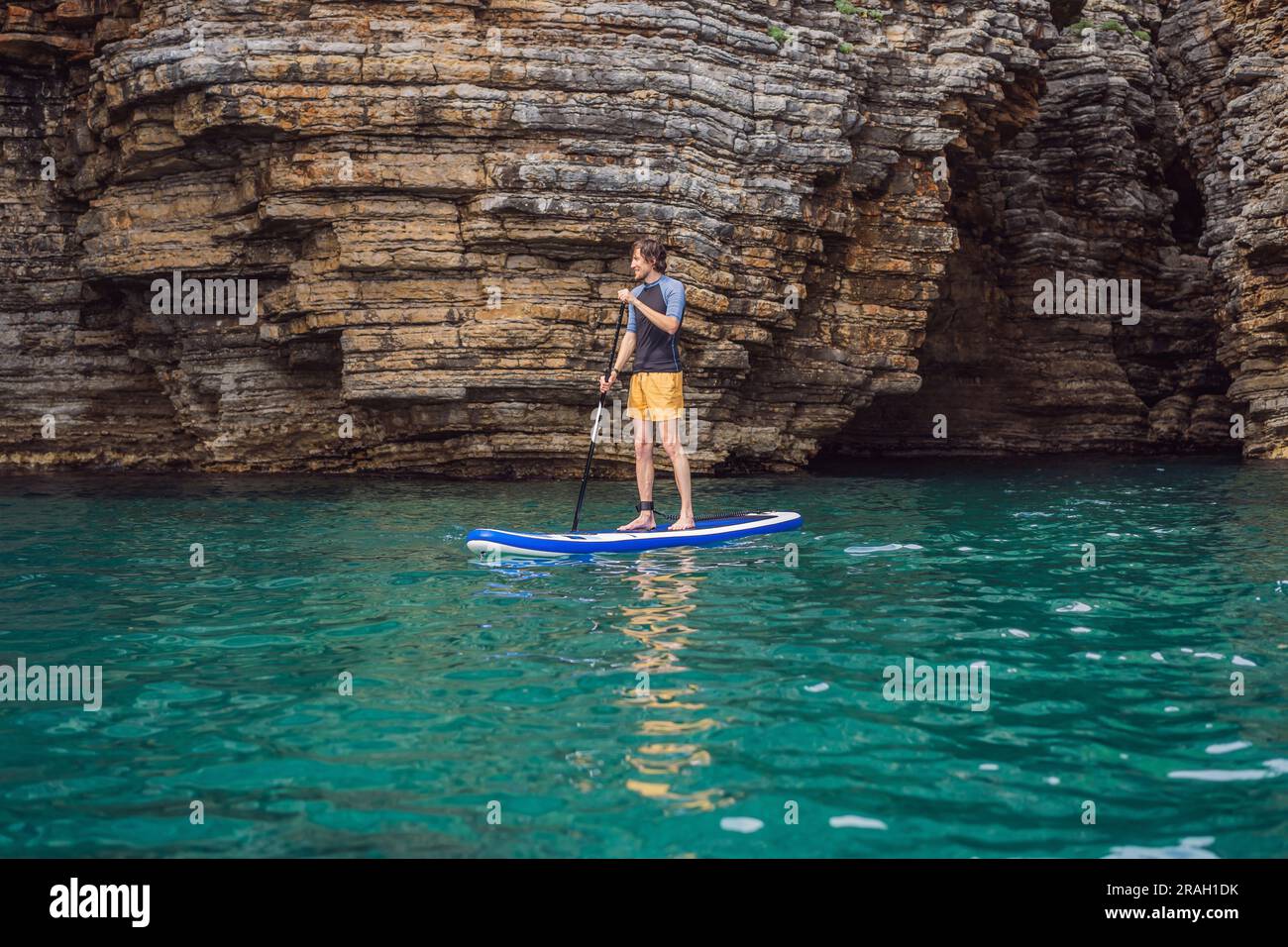 Young men Having Fun Stand Up Paddling in blue water seaamong the rocks