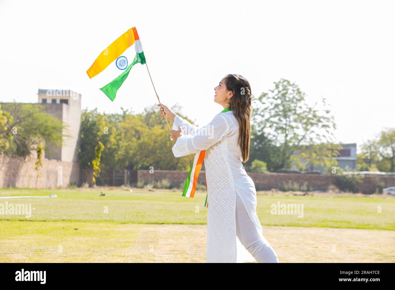 Young beautiful woman wearing traditional white dress holding indian and weaving flag while standing at park celebrating Independence day or Republic Stock Photo