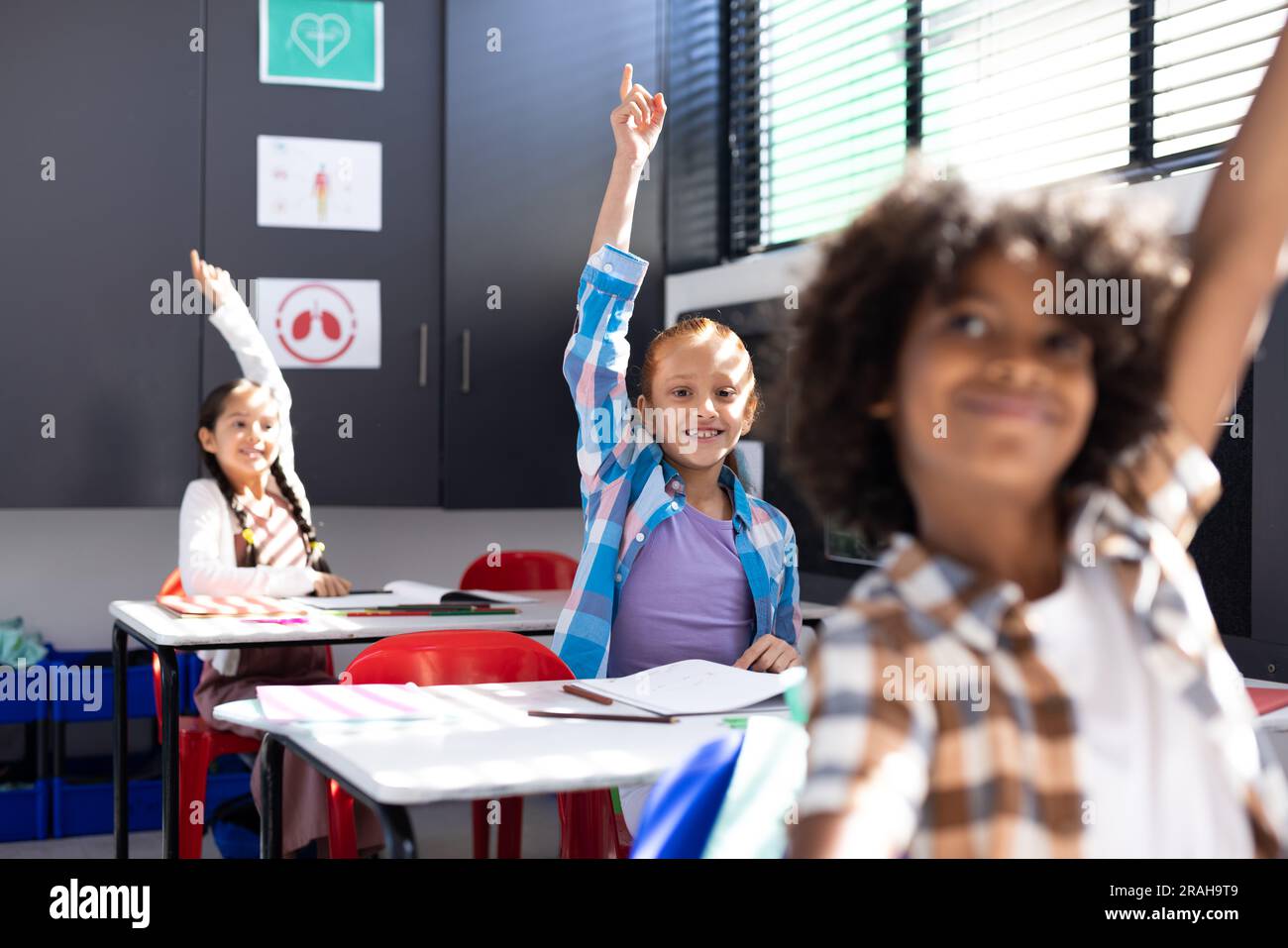 Diverse, happy children sitting at desks raising hands in elementary ...