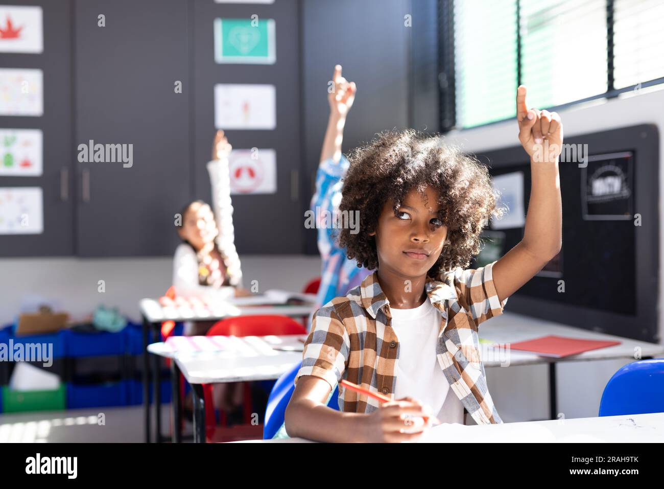African american boy sitting at desk raising hand in elementary school ...