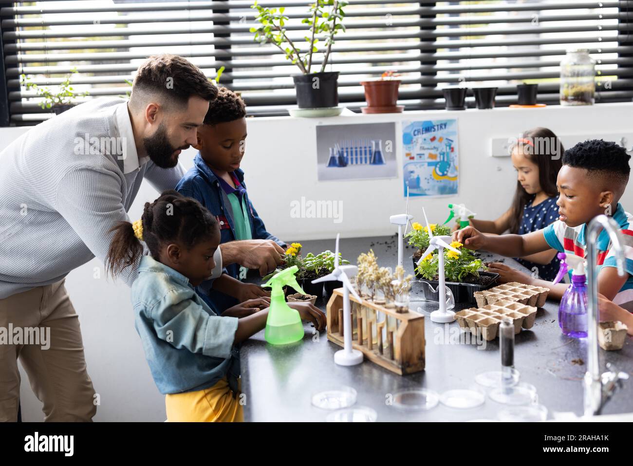 Diverse elementary schoolchildren and male teacher studying plants ...