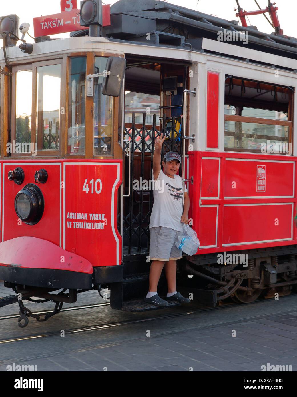 Boy waves from the red Heritage Tram aka Trolley aka Streetcar in Taksim Square, Istanbul Turkey, on a summers evening. Stock Photo