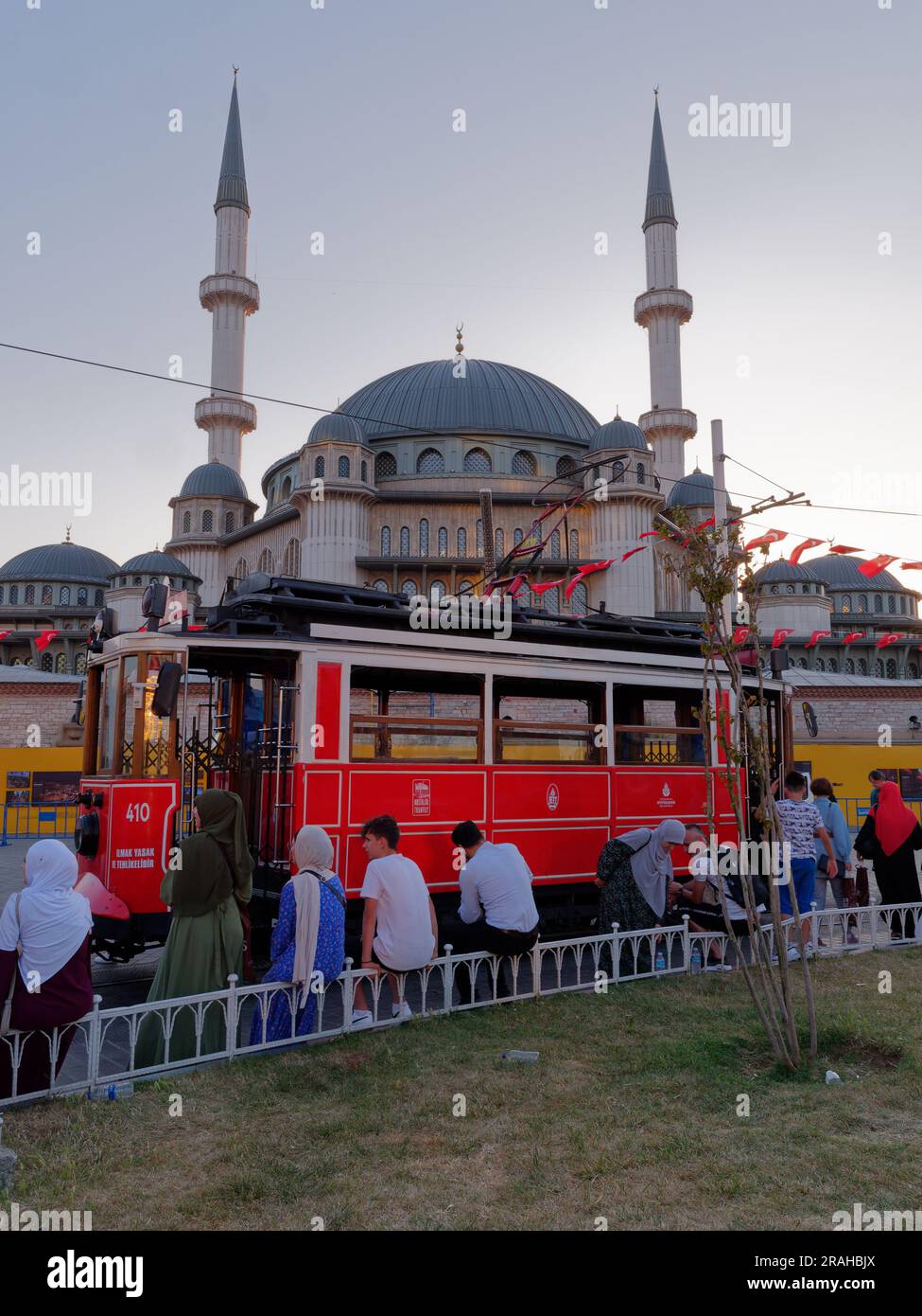 People sit in Taksim Square on a summers evening, with the red Heritage Tram and Taksim Mosque, Istanbul, Turkey Stock Photo