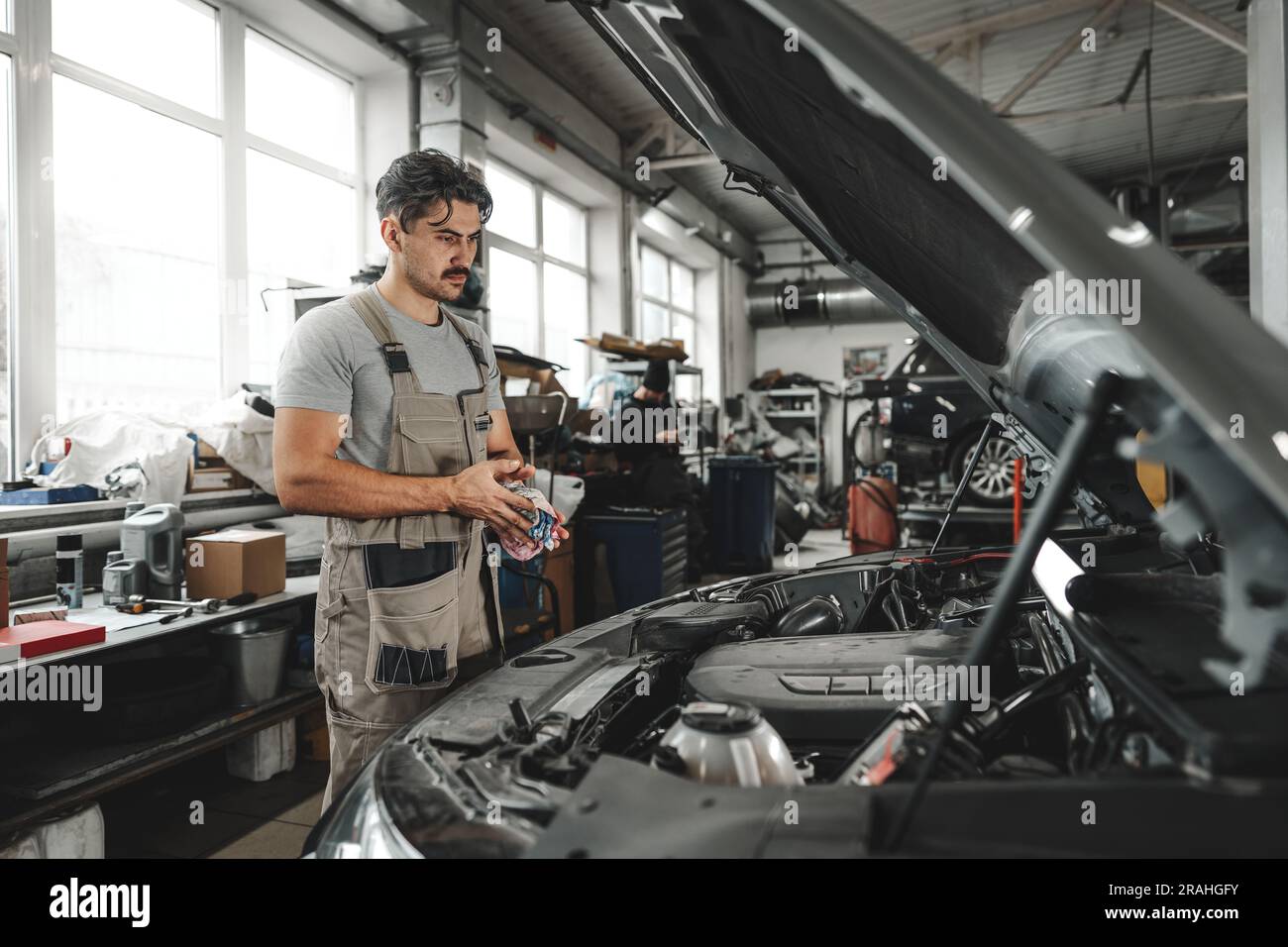 Young male mechanic examining engine under hood of car at the repair ...