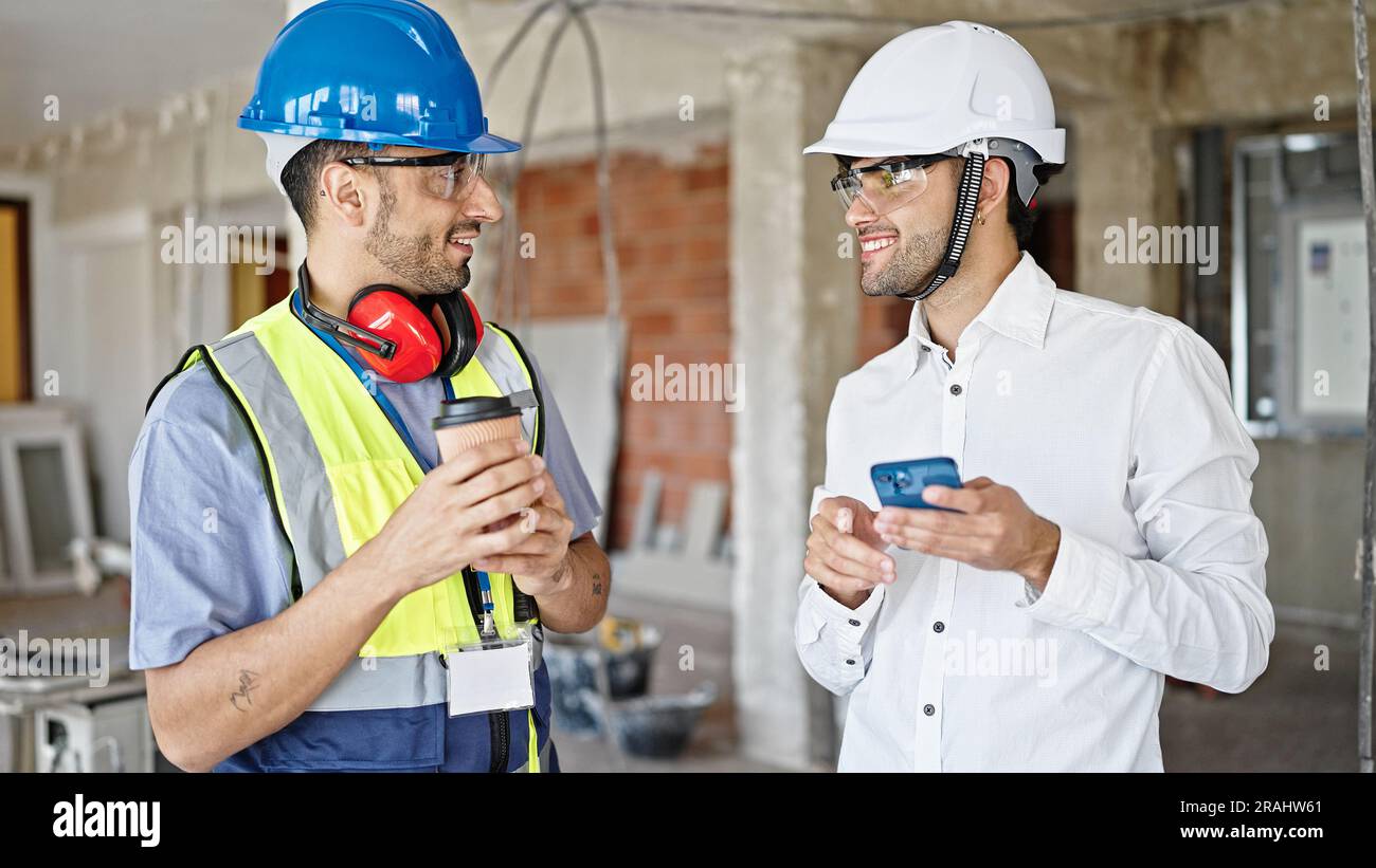 Two men builder and architect using smartphone drinking coffee at construction site Stock Photo