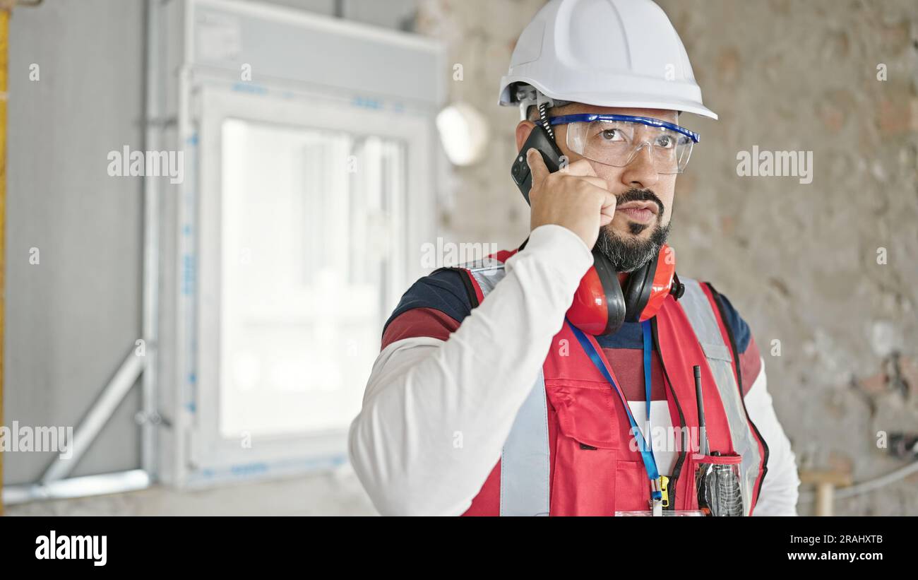 Young latin man builder talking on smartphone at construction site Stock Photo