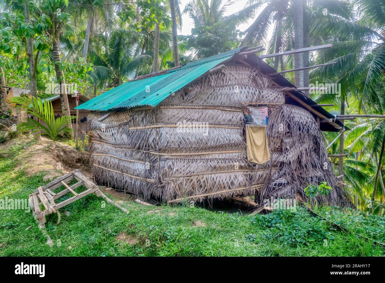 A thatched house with a corrugated metal roof built on the edge of a hill in rural Oriental Mindoro Province, Philippines, a wooden water buffalo sled. Stock Photo