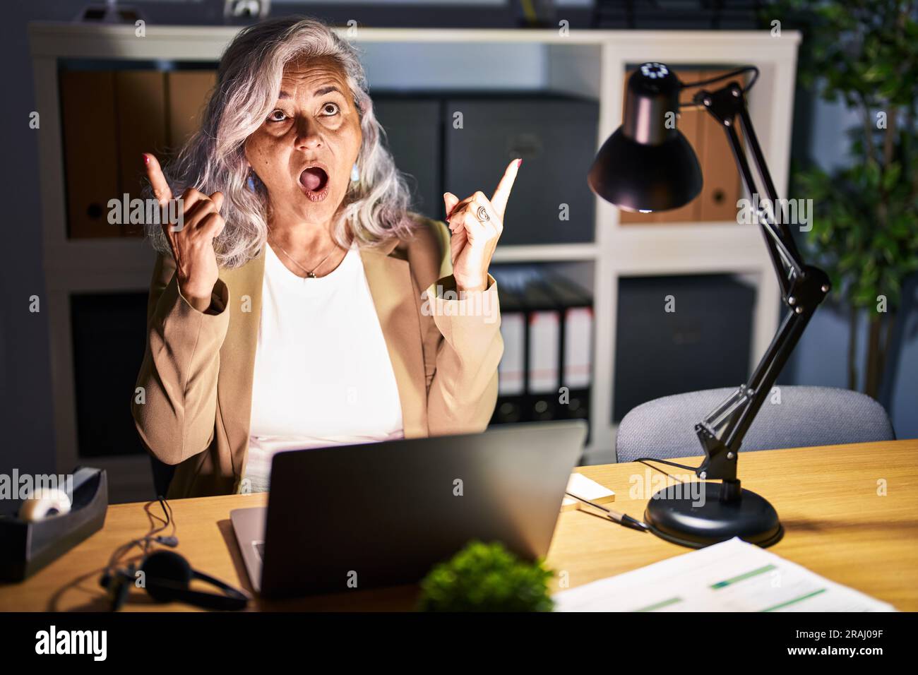 Middle age woman with grey hair working using computer laptop late at ...