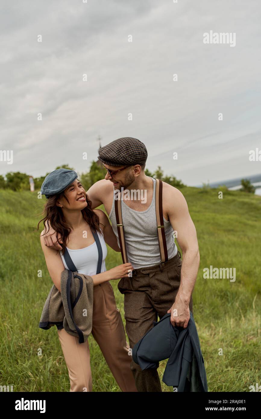 Fashionable bearded man in sunglasses and newsboy cap hugging cheerful ...