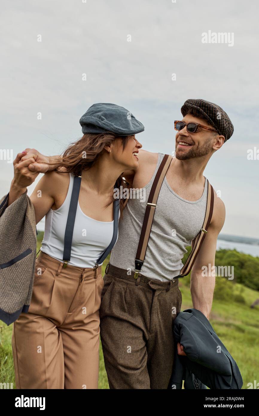Smiling bearded man in vintage outfit and newsboy cap hugging brunette ...
