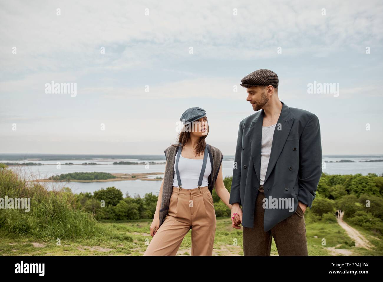 Fashionable and bearded man in newsboy cap and jacket holding hand of ...