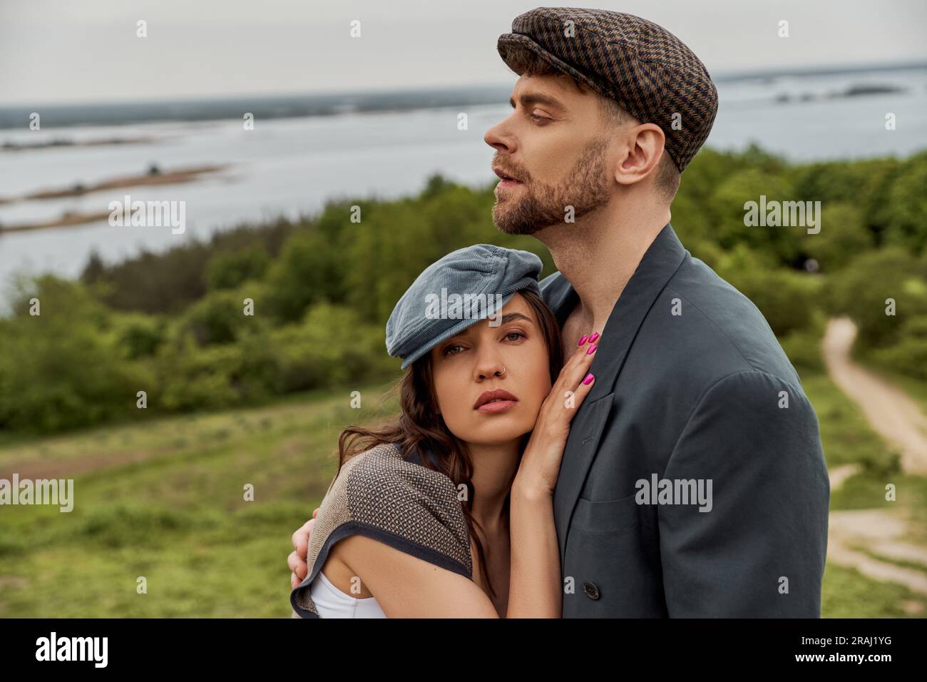 Brunette and fashionable woman in newsboy cap and vest hugging bearded ...