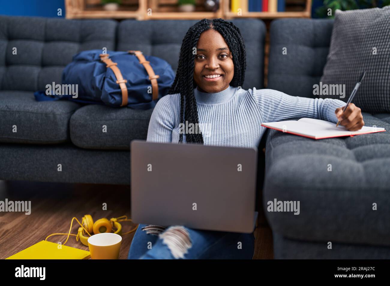 African american woman student using laptop writing on notebook at ...