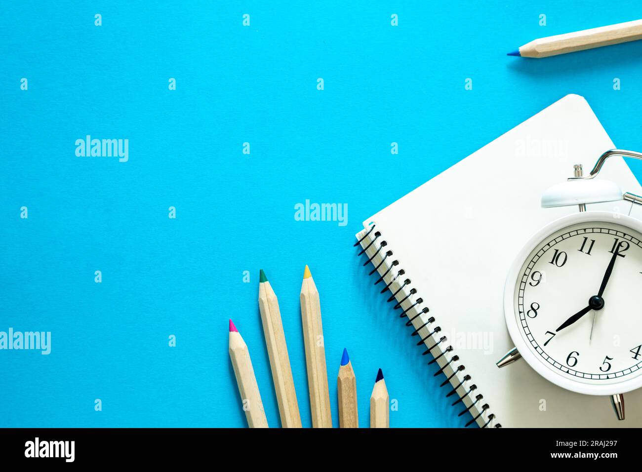 Notebook, pencils and an alarm clock on a blue background, top view ...