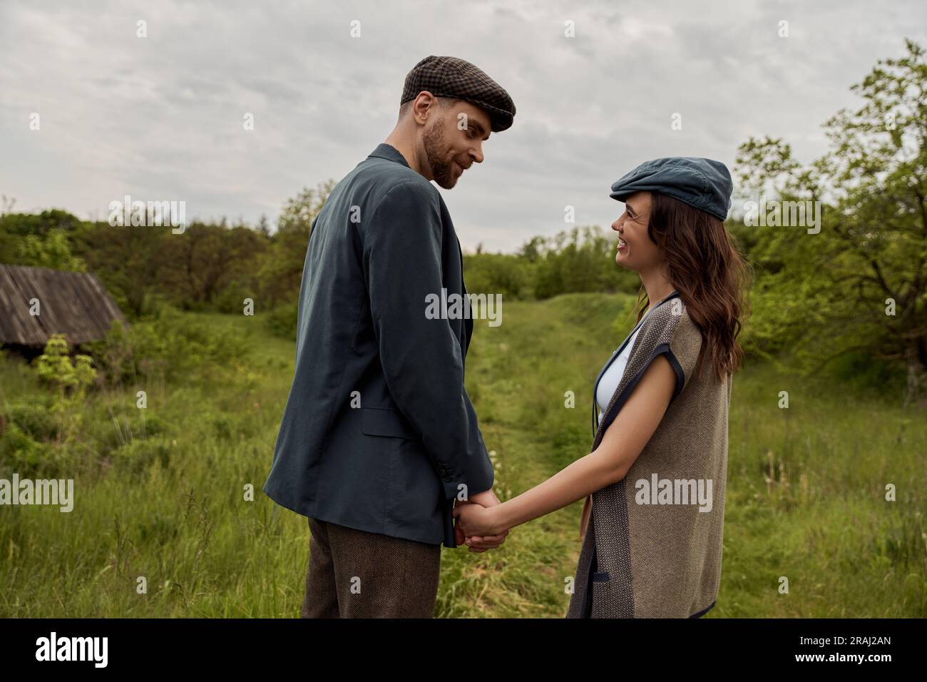 Bearded and stylish man in jacket and newsboy cap holding hand and ...