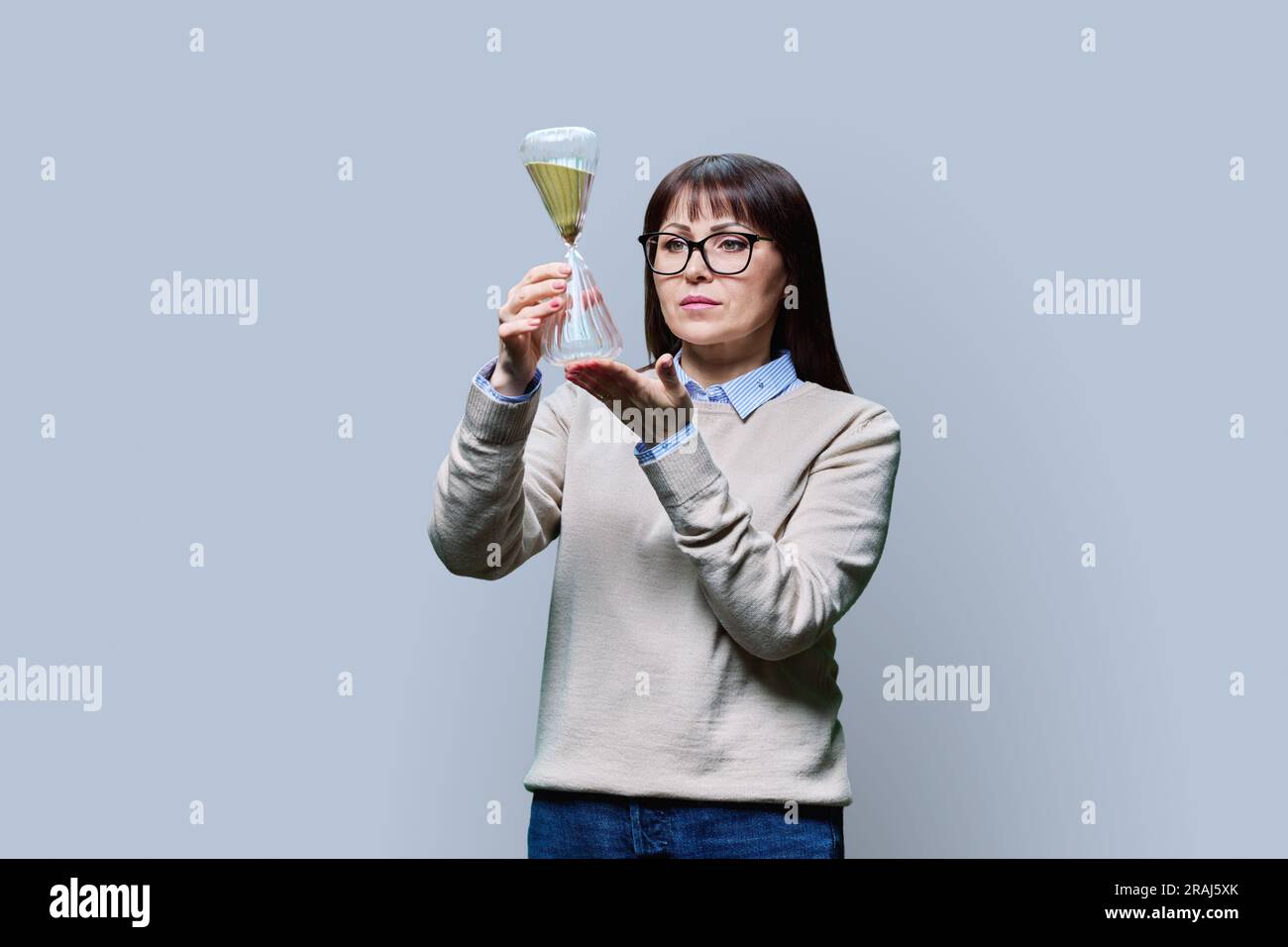 Middle aged woman with hourglass on grey studio background Stock Photo