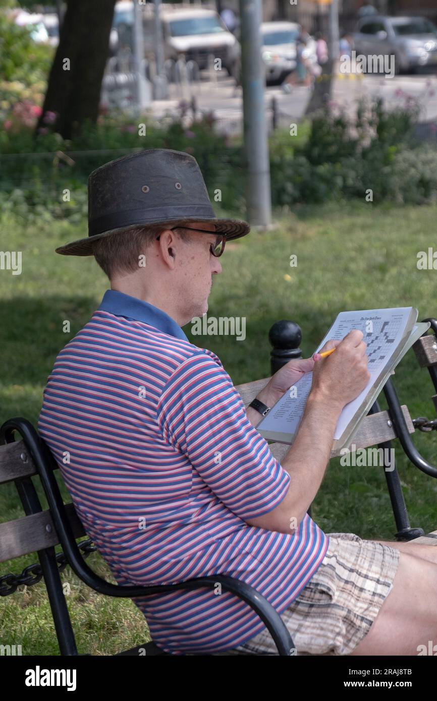 Doing the New York Times daily crossword puzzle on a bench in Washington Square Park in lower Manhattan. Stock Photo