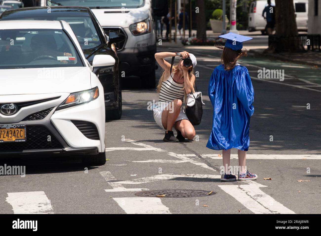 A young girl in a blue cap and gown is photographed on Fifth Avenue in New York City, June 2023. It may be mother & daughter. Stock Photo