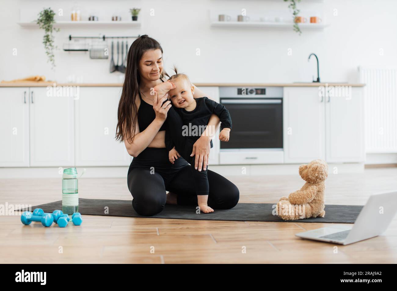 Adorable little child doing splits with mother's support while following  on-screen instructor at home. Happy caucasian ladies in black wear enjoying  baby yoga without leaving comfort of room Stock Photo - Alamy