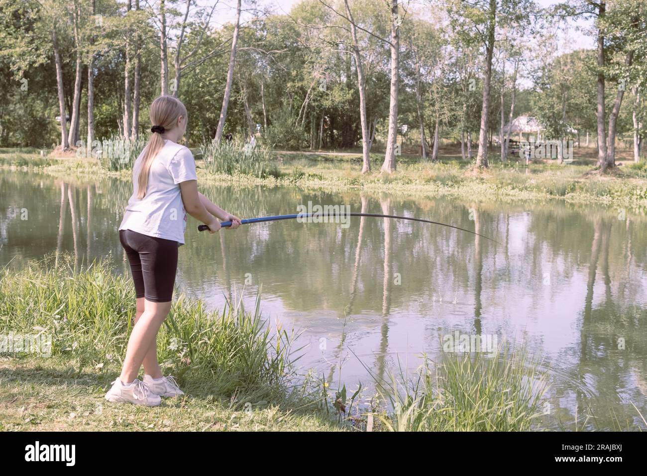 https://c8.alamy.com/comp/2RAJBXJ/a-teenager-girl-of-european-appearance-with-blond-hair-tied-in-a-ponytail-stands-fishing-at-a-stake-holds-a-fishing-rod-in-her-hands-dressed-in-bla-2RAJBXJ.jpg