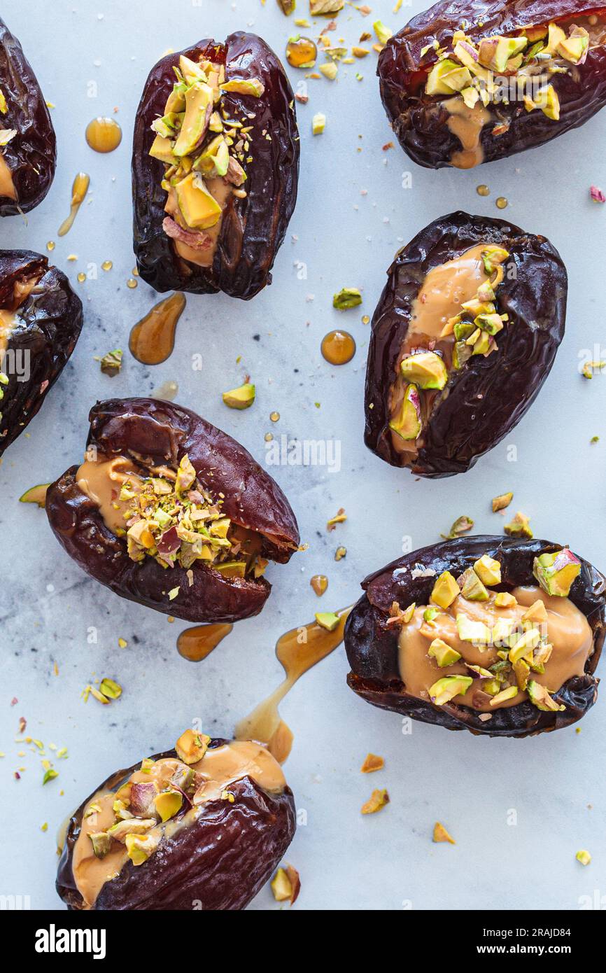 Dates stuffed with peanut butter and pistachios on a white marble background. Vegan dessert, healthy snack recipe. Stock Photo