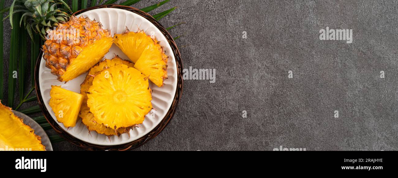 Top view of fresh cut pineapple with tropical leaves on dark gray table background. Stock Photo
