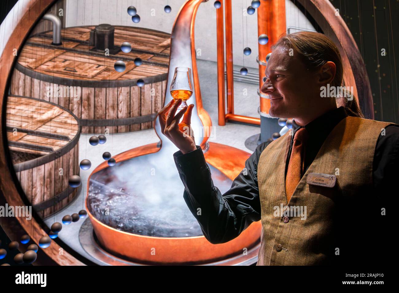 Tour guide with glass of whisky at immersive visitor media image projection about whisky brewing