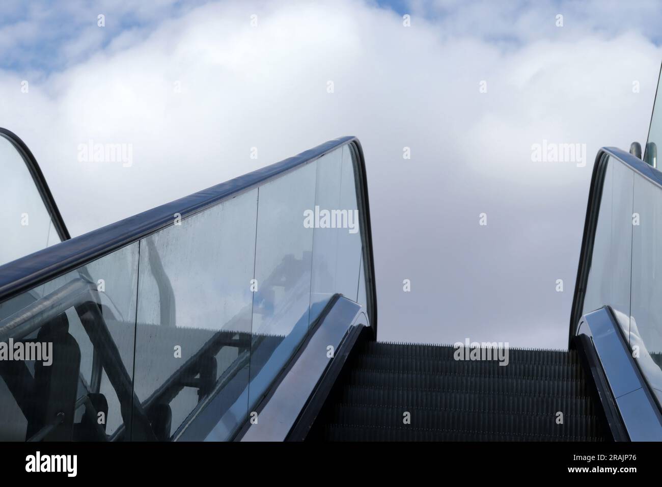 Open air escalator raise towards sunny blue sky with white clouds. Stock Photo