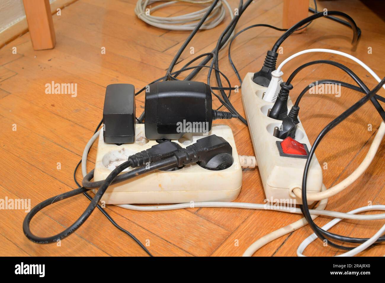 Tangled cables on the parquet floor. Overloaded electrical boards on