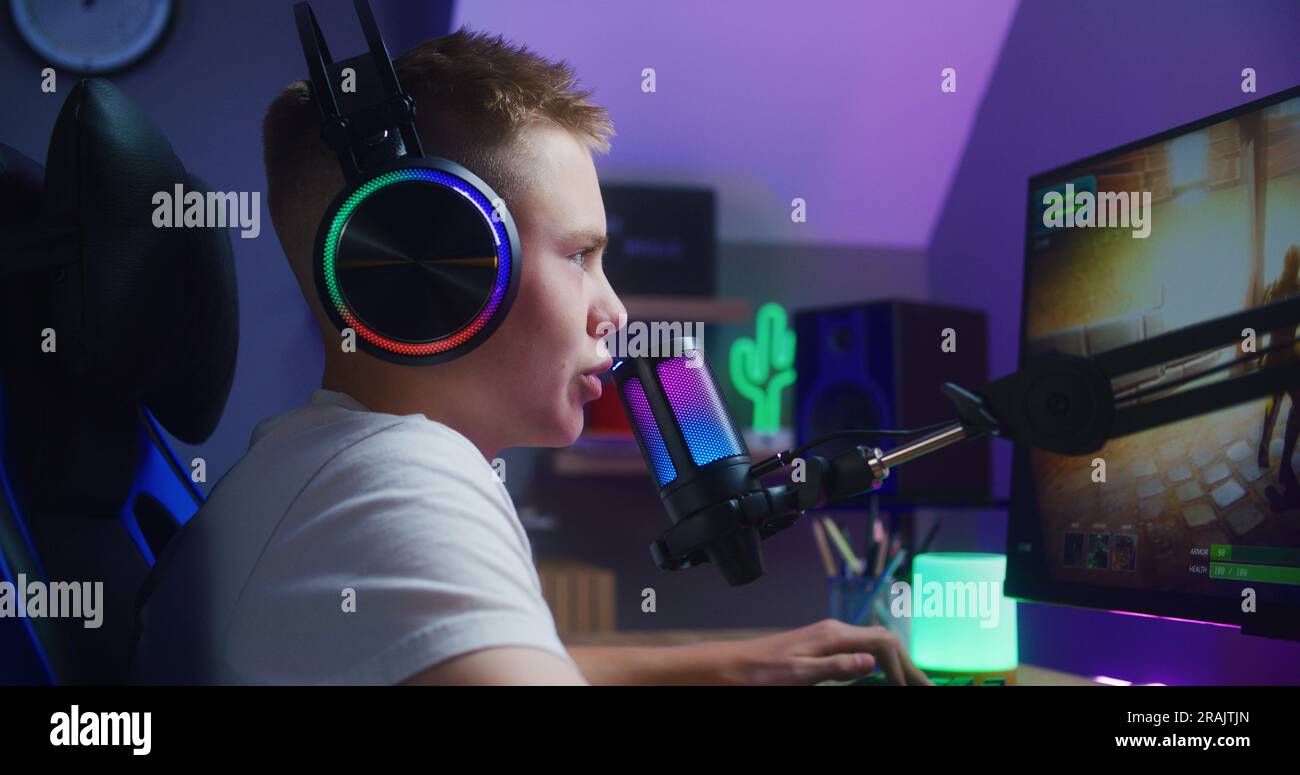 Young gamer in headphones talks with teammates and plays in third person shooter on computer at home