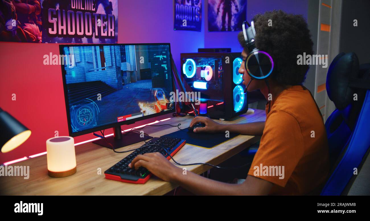 African American teenage gamer in headphones plays and loses round in online first-person 3D shooter on modern PC in neon room