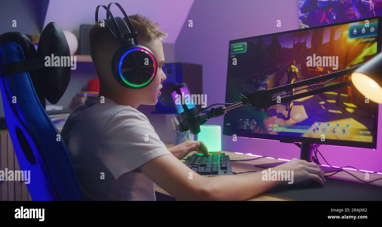 Young gamer in headphones talks with teammates and plays in third ...