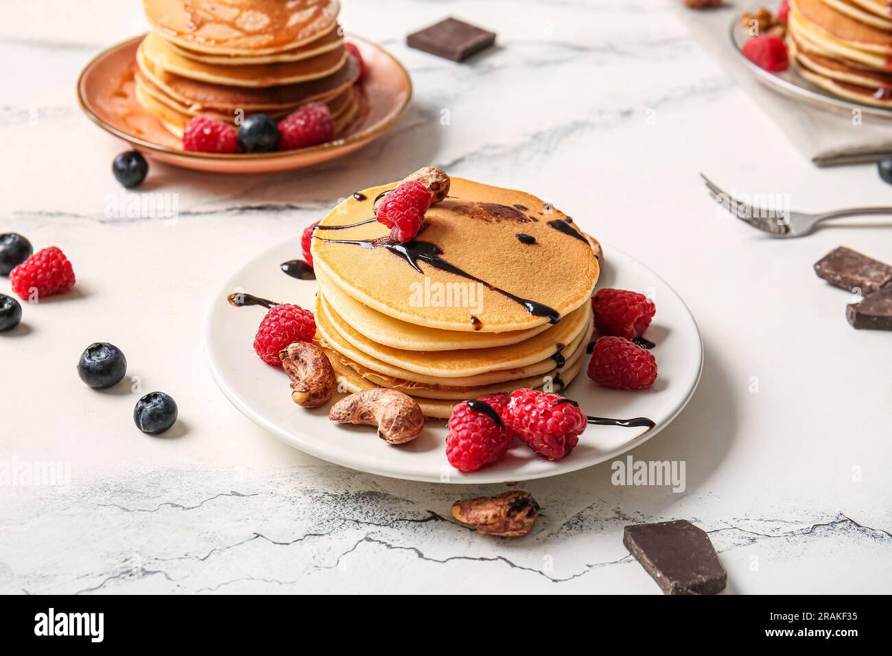 Plates of tasty pancakes with raspberries, blueberries and nuts on white marble background Stock Photo
