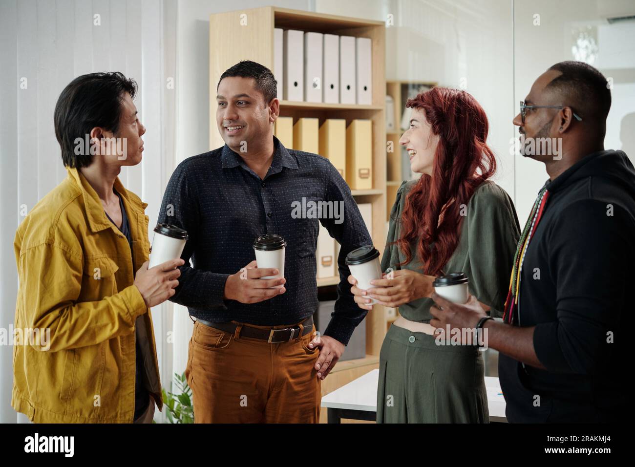 Friendly cheerful colleagues drinking coffee and discussing weekend in office Stock Photo