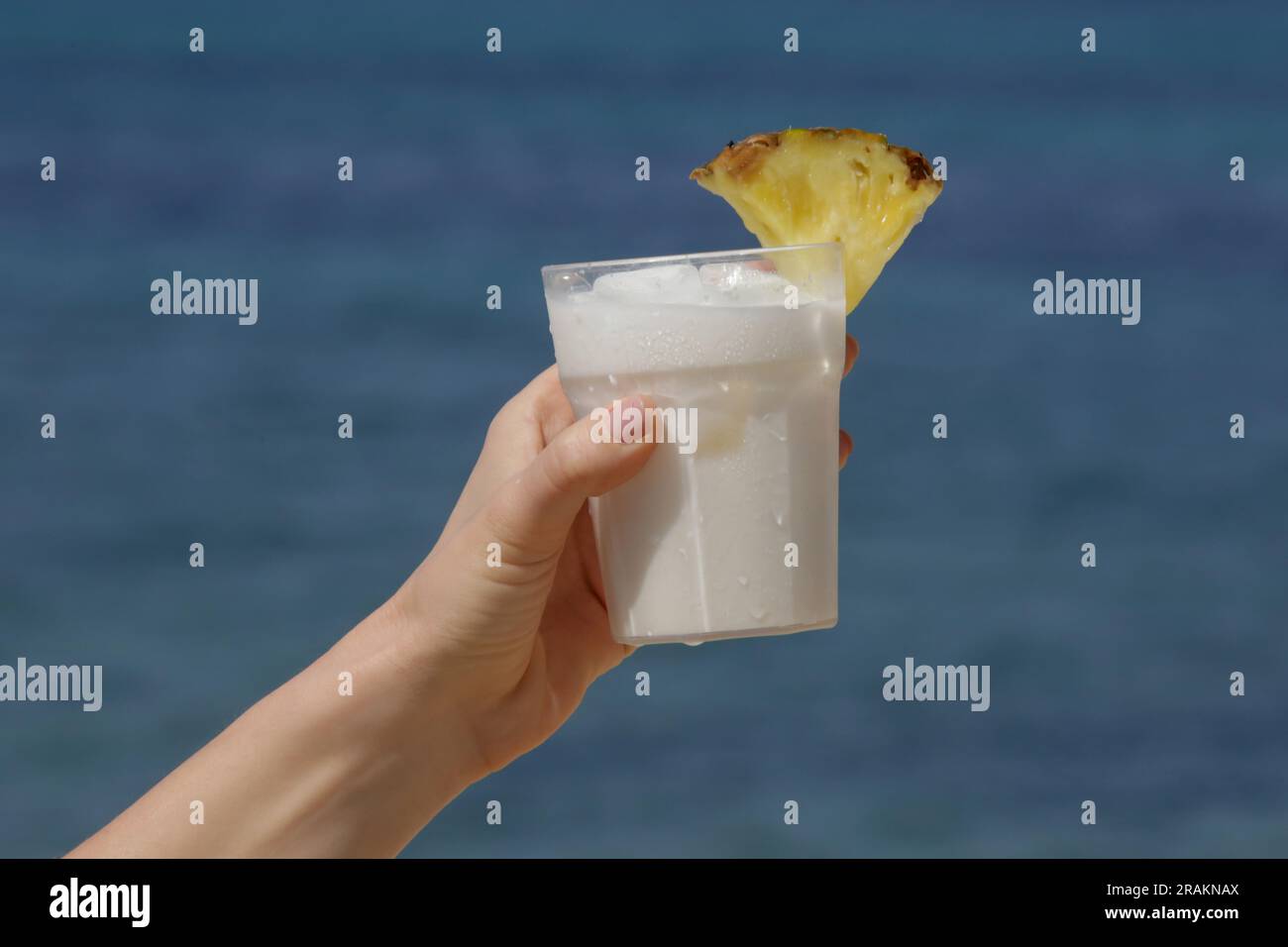 Woman hand with Pina colada cocktail with beach behind Stock Photo
