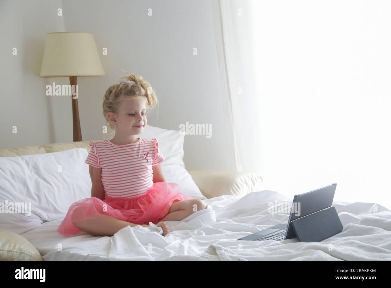 Child sitting on bed watching cartoons on digital tablet Stock Photo
