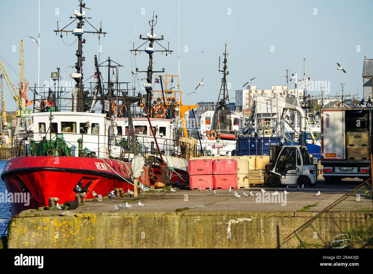Liepaja, Latvia- May 06, 2023: Colorful harbor view with fishing vessels, fish containers and seagulls on blue sky background Stock Photo