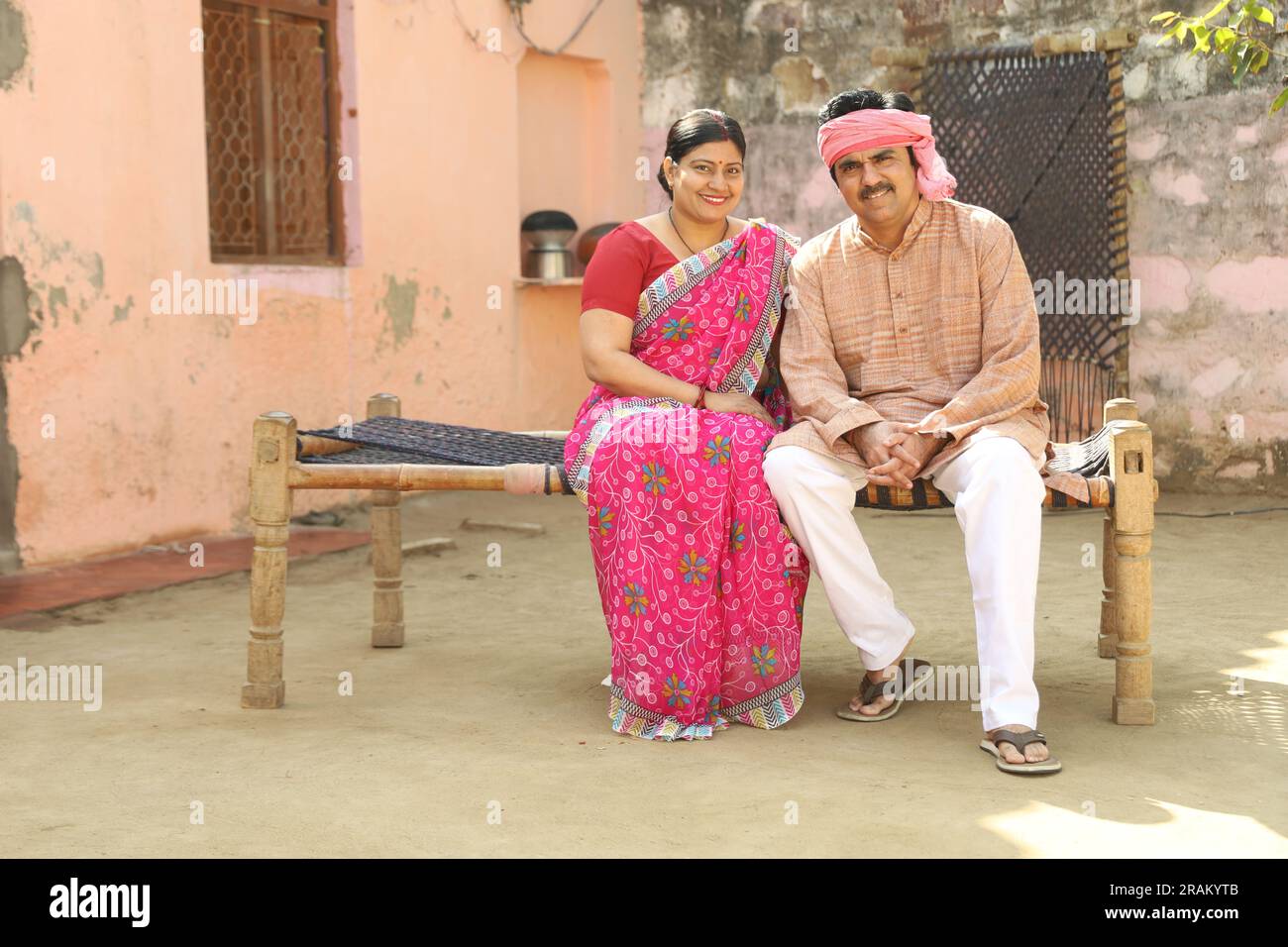 Indian rural farmer couple sitting outdoors together. Indian villager's attire. husband and wife sitting on cot. Rural Indian man and woman. Stock Photo