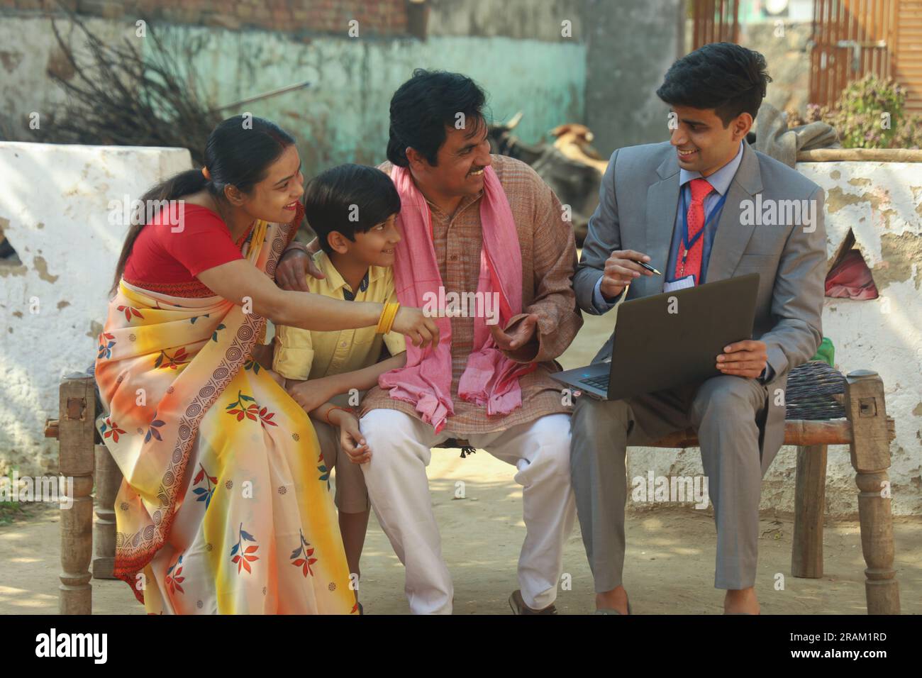 Happy Indian village family sitting with the banker or financial consultant using the laptop sitting outside the house. Education loan Stock Photo