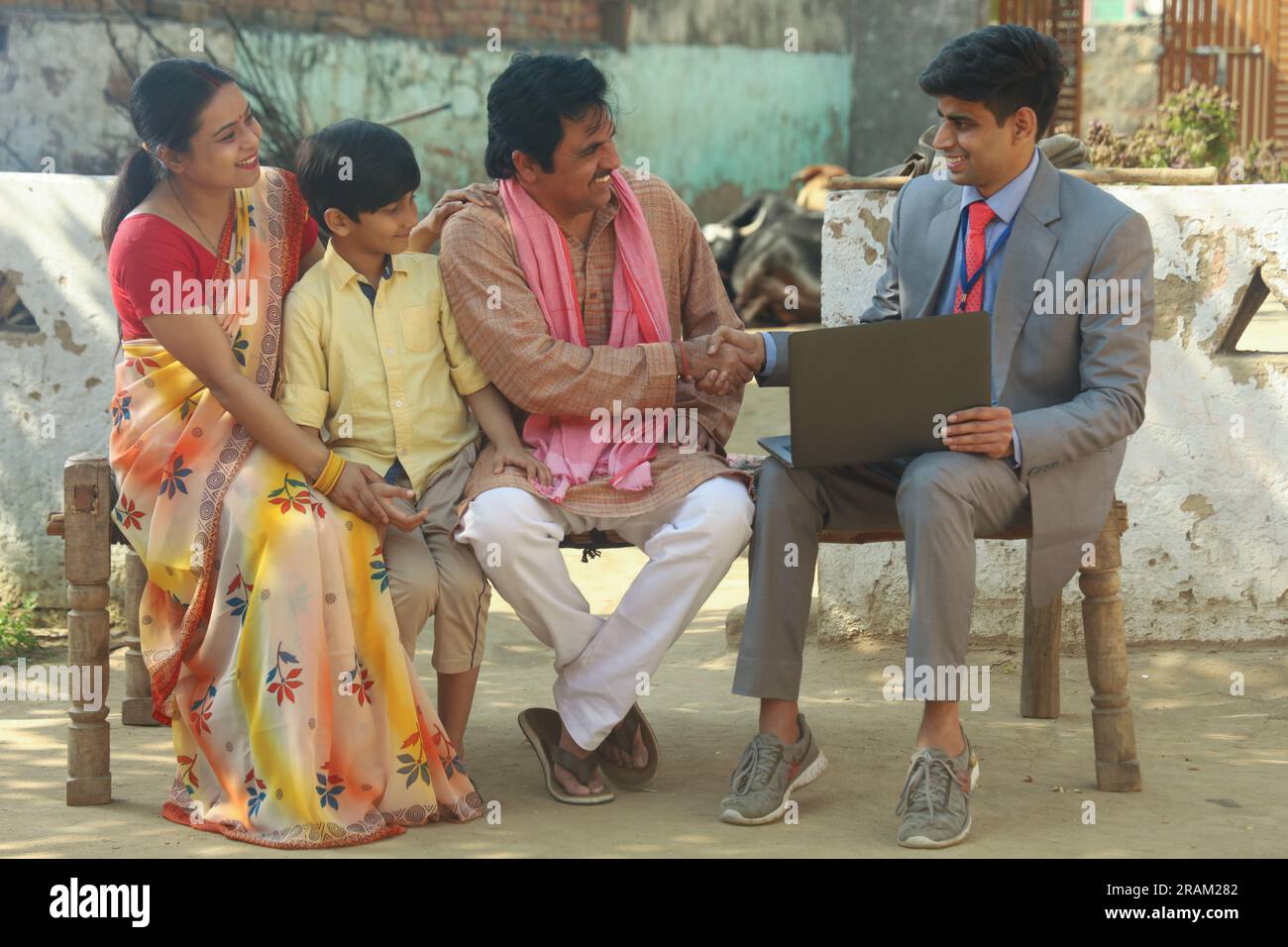 Happy Indian village family sitting with the banker or financial consultant using the laptop sitting outside the house. Education loan Stock Photo