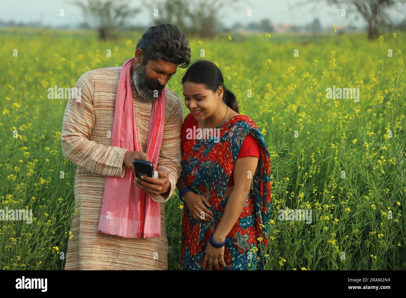 Young happy Indian farmer couple standing in mustard field holding ...