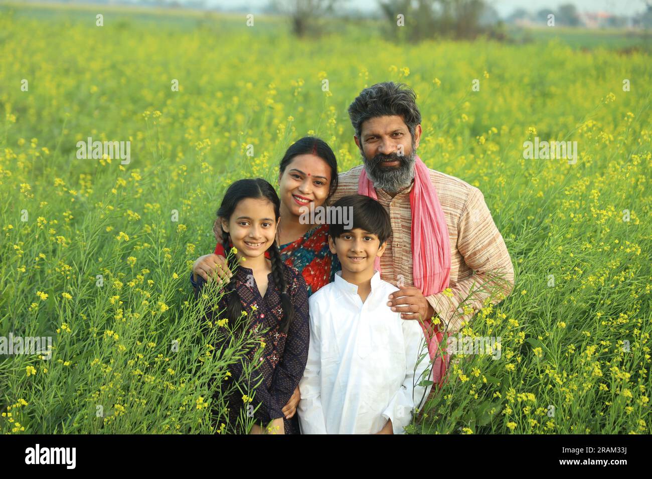 Happy Indian farmers family standing in mustard field in day time ...