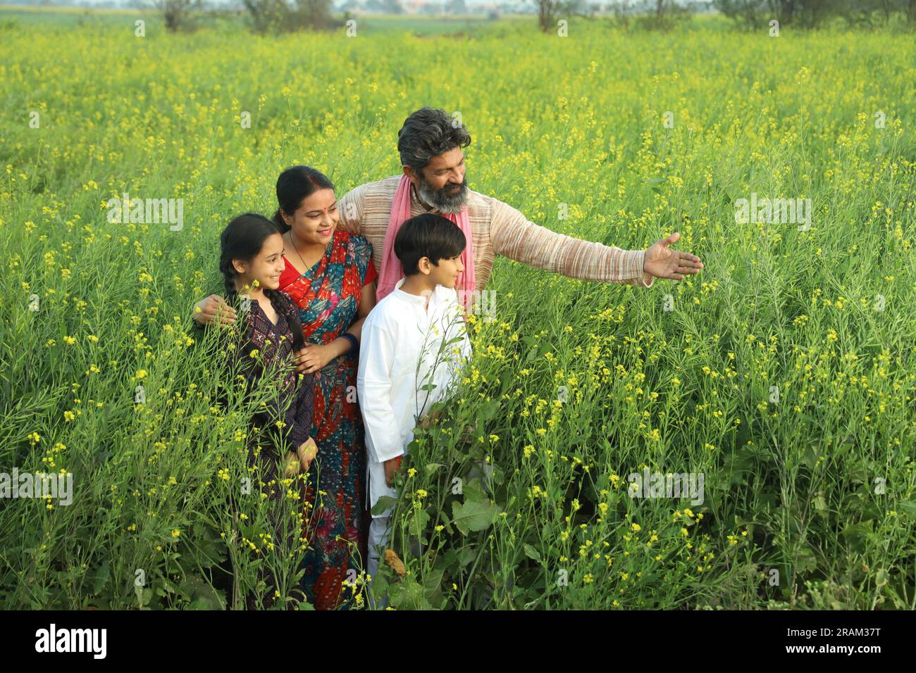 Happy Indian farmers family standing in mustard field in day time ...