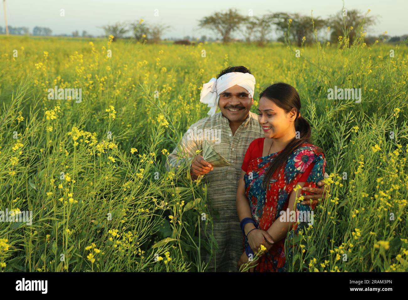Young happy Indian farmer couple standing in mustard field in a day ...