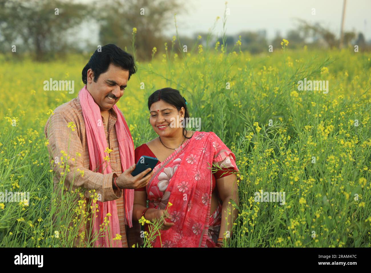 Young happy Indian farmer couple standing in mustard field holding ...