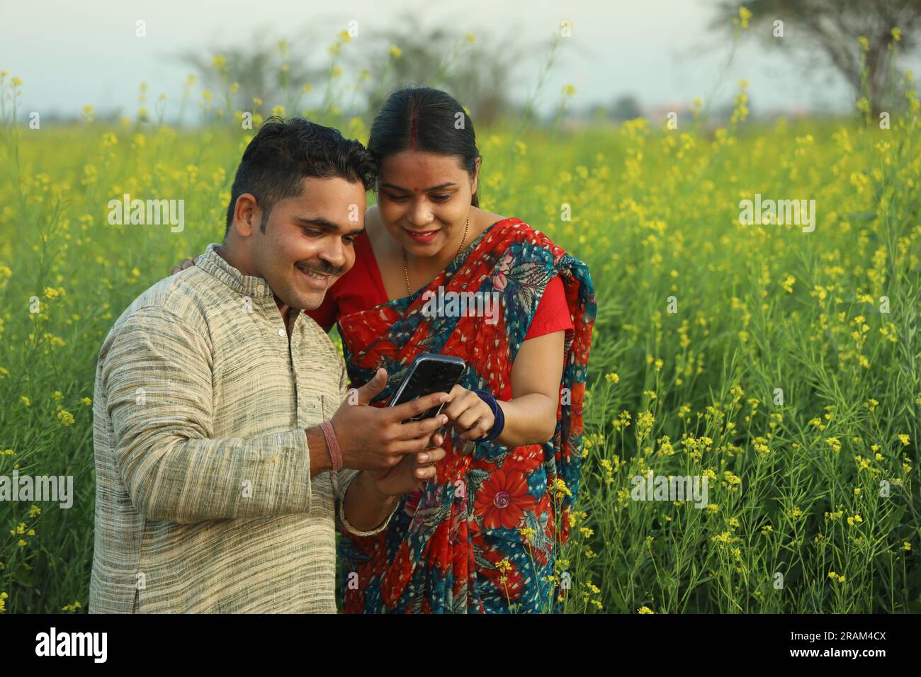 Young happy Indian farmer couple standing in mustard field holding ...
