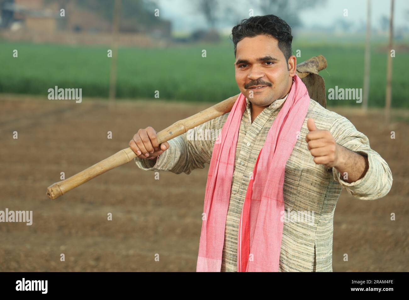 Portrait of Indian happy farmer ploughing the field manually in a day time. Holding agricultural tool in hand. Digging tool shovel and hoe in hand. Stock Photo